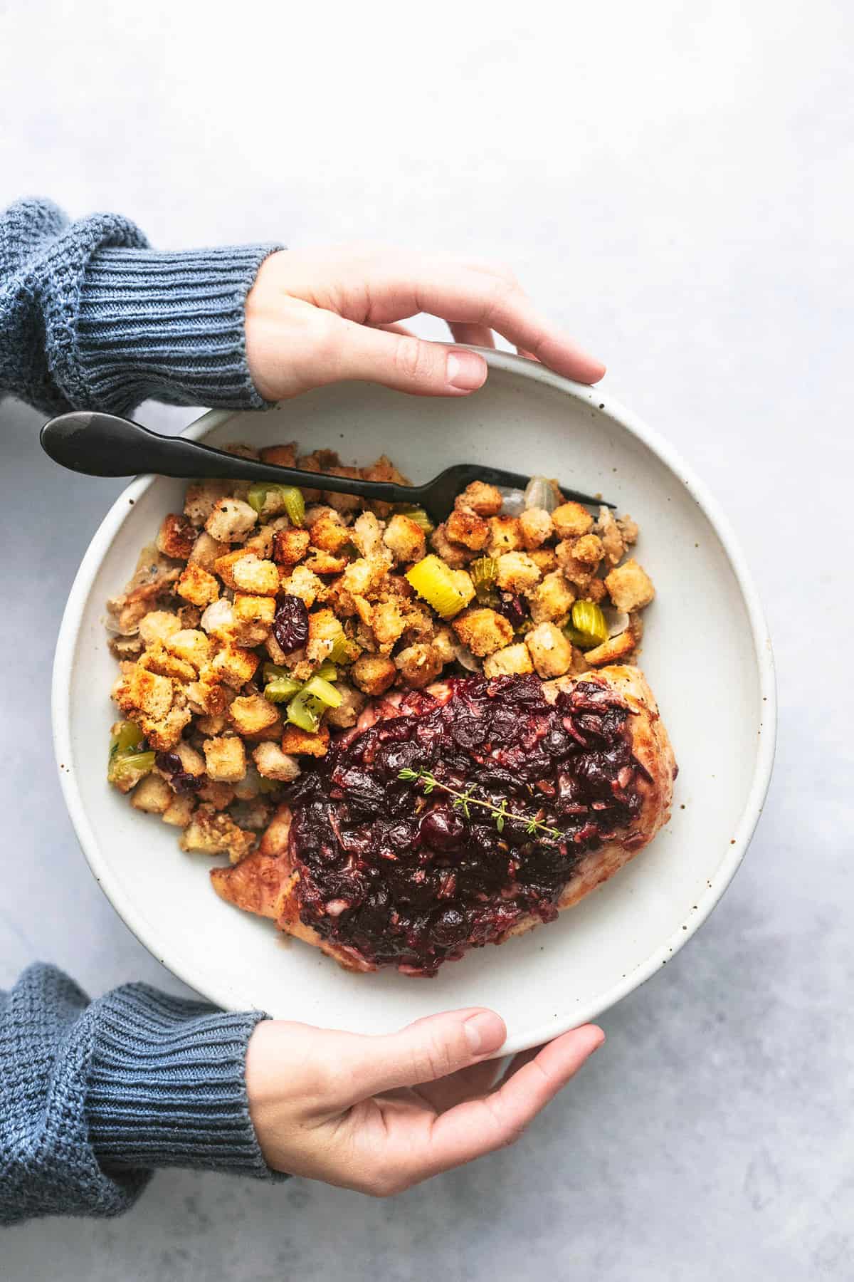 top view of hands holding a plate with sheet pan cranberry chicken and stuffing and a fork on it.