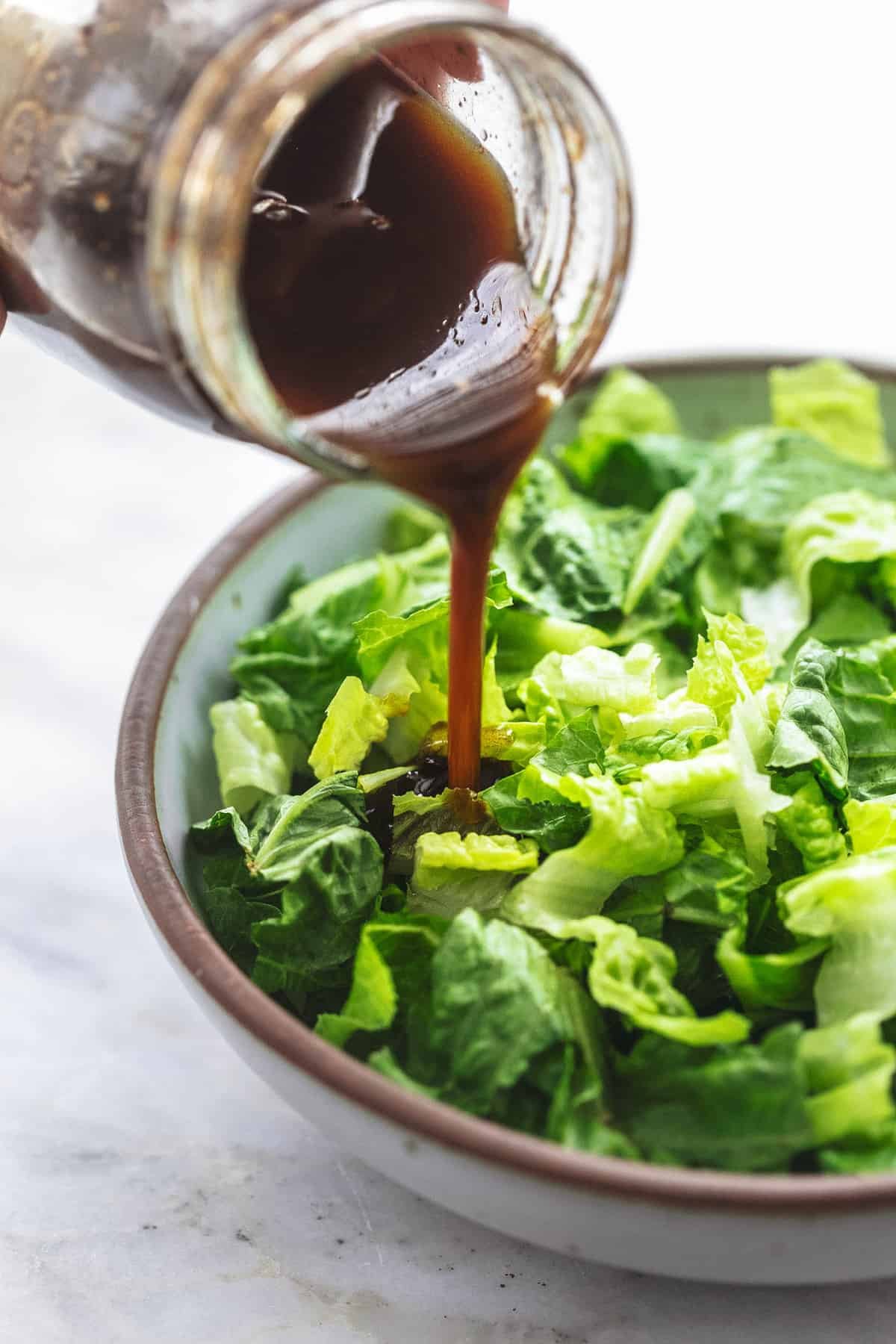 balsamic vinaigrette salad dressing being poured from a jar onto salad in a bowl.