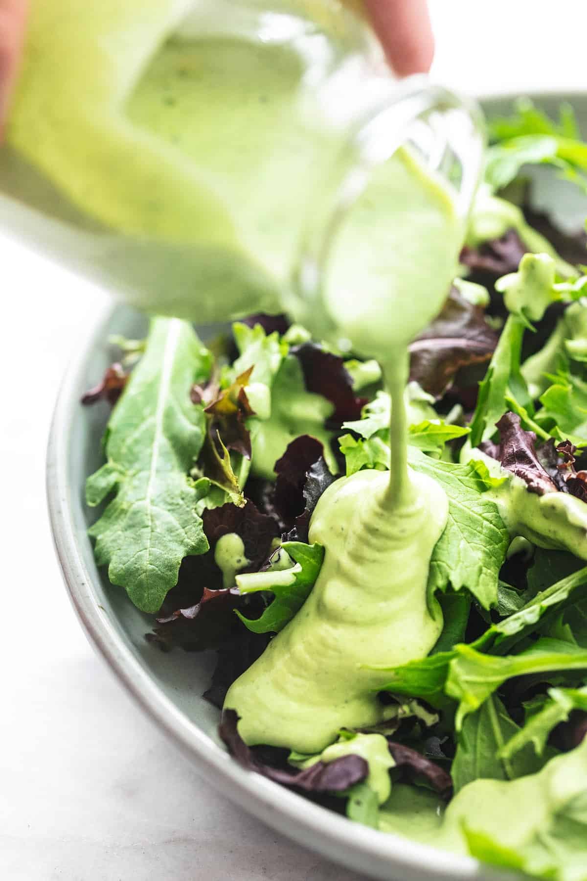 close up of cilantro avocado ranch dressing being poured out of a jar onto salad in a bowl.