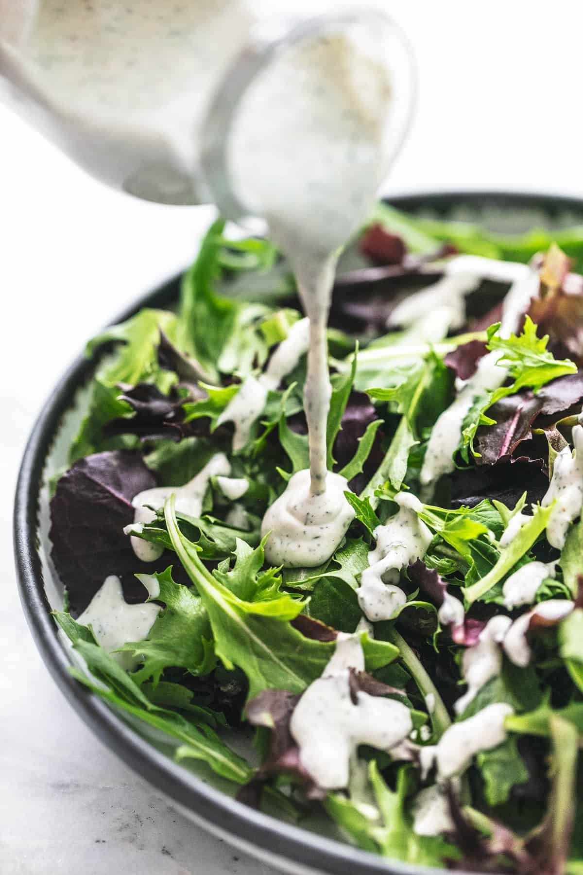 a jar of Greek yogurt ranch dressing or dip being poured onto salad in a bowl.
