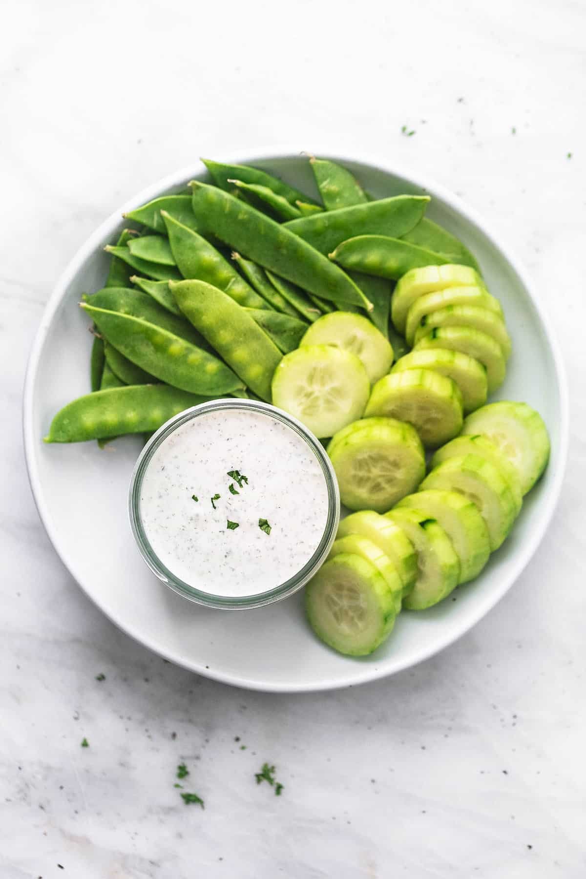 top view of Greek yogurt ranch dressing or dip in a jar with cucumber slices and pea pods on the side all on a plate.