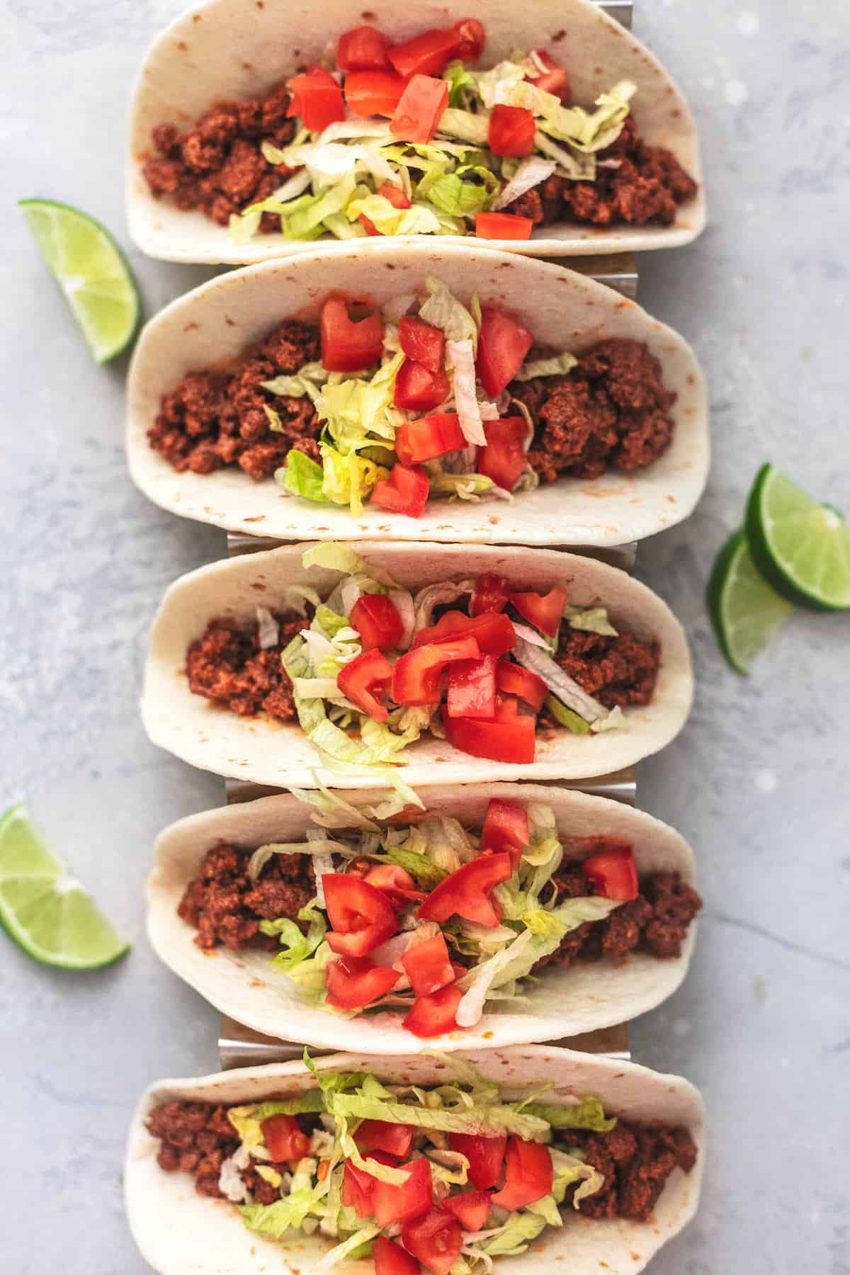 top view of ground beef tacos with toppings on them in a taco holder with lime slices on the side.