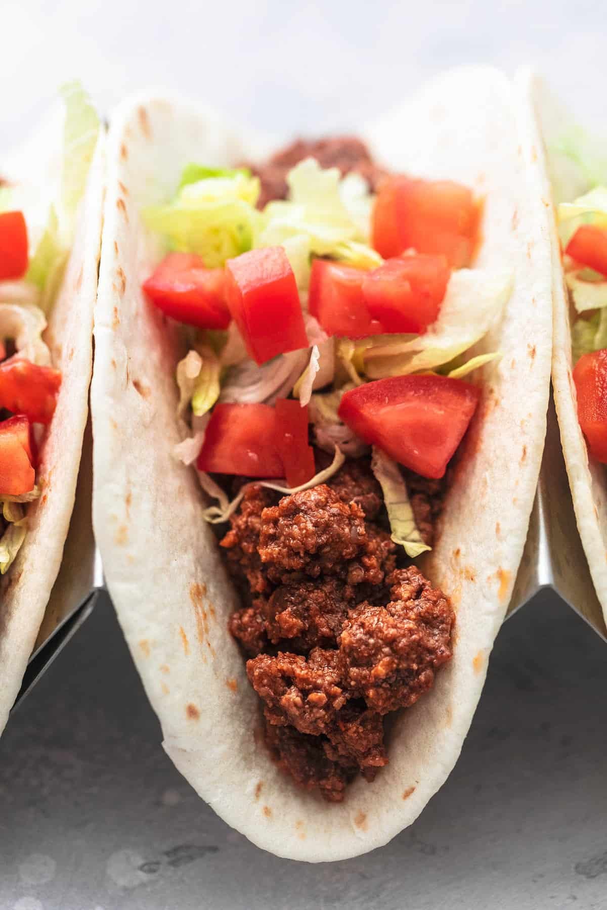 close up of a ground beef taco with toppings in a taco holder with more tacos on the sides.