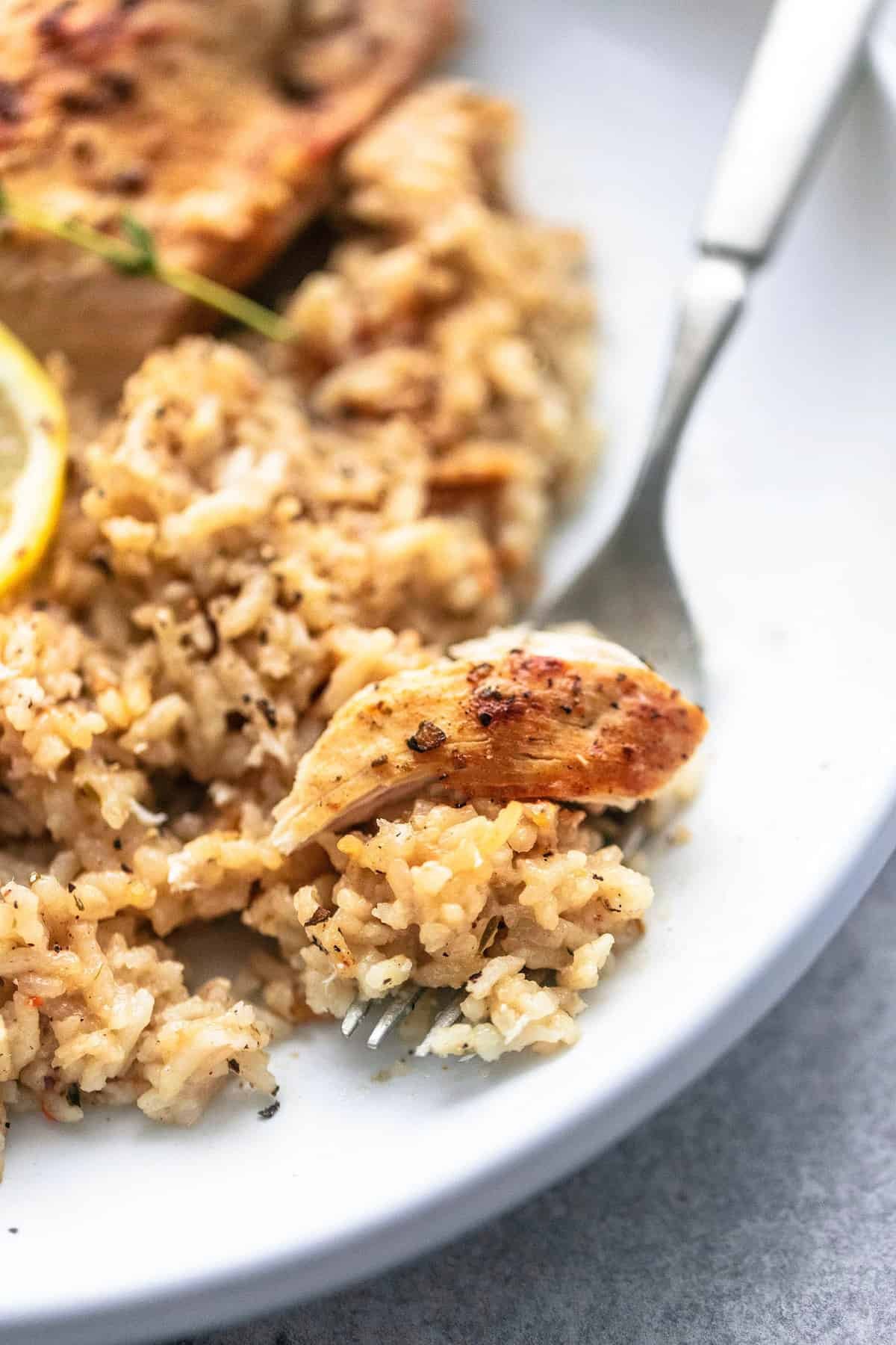 close up of a bite of instant pot chicken breast and rice on a fork with more on the side all on a plate.