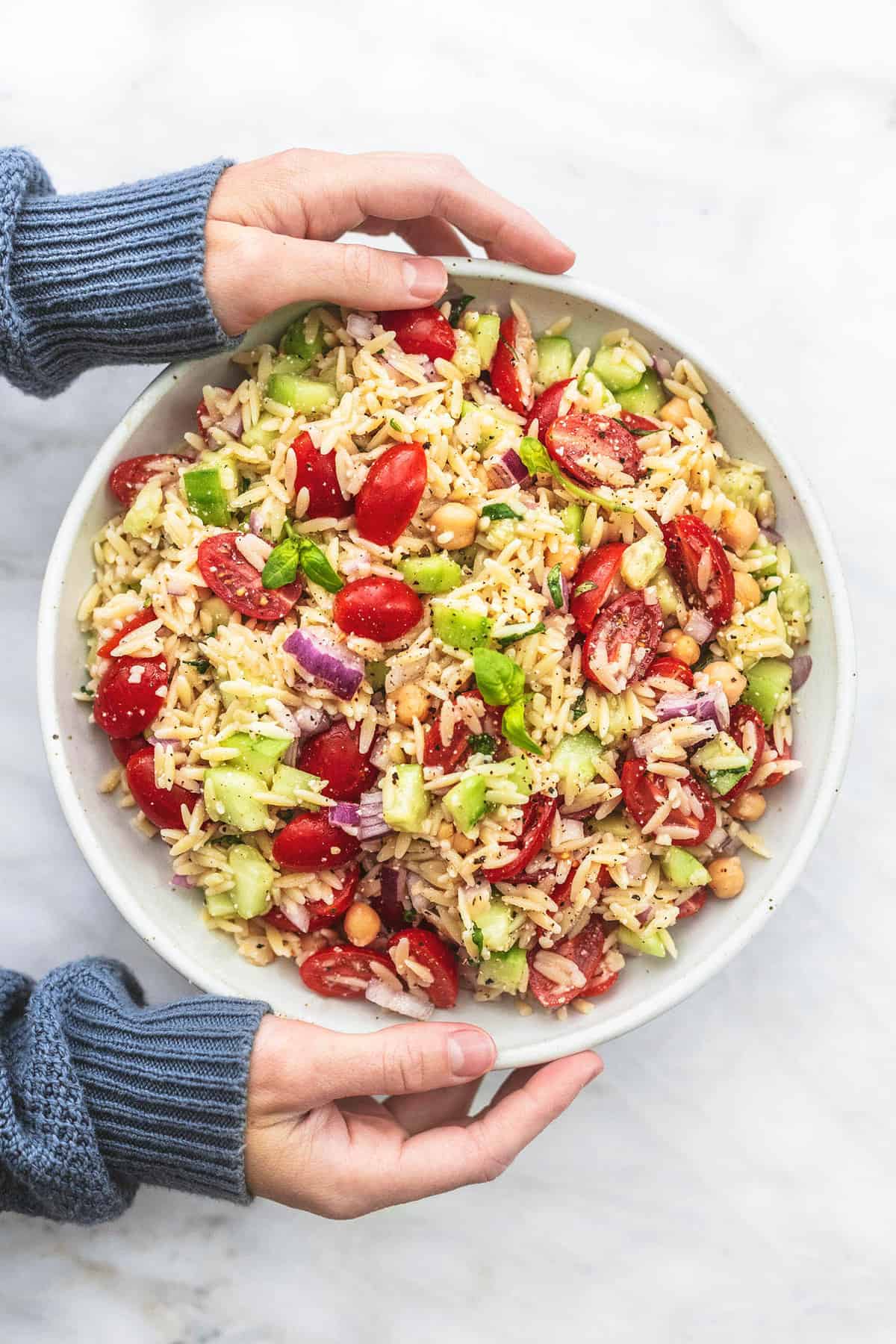 top view of a pair of hands holding a bowl of Italian orzo salad.
