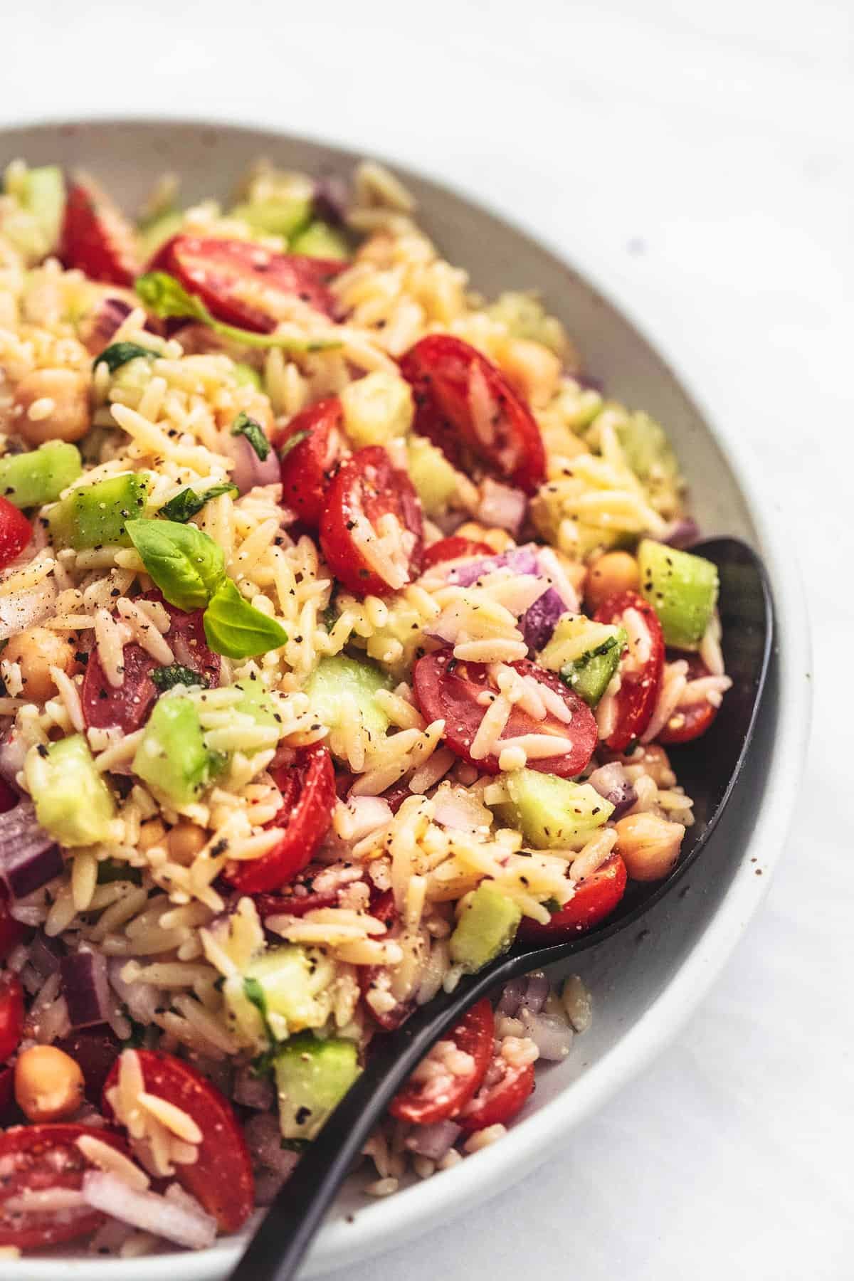 close up of Italian orzo salad with a serving spoon in a bowl.