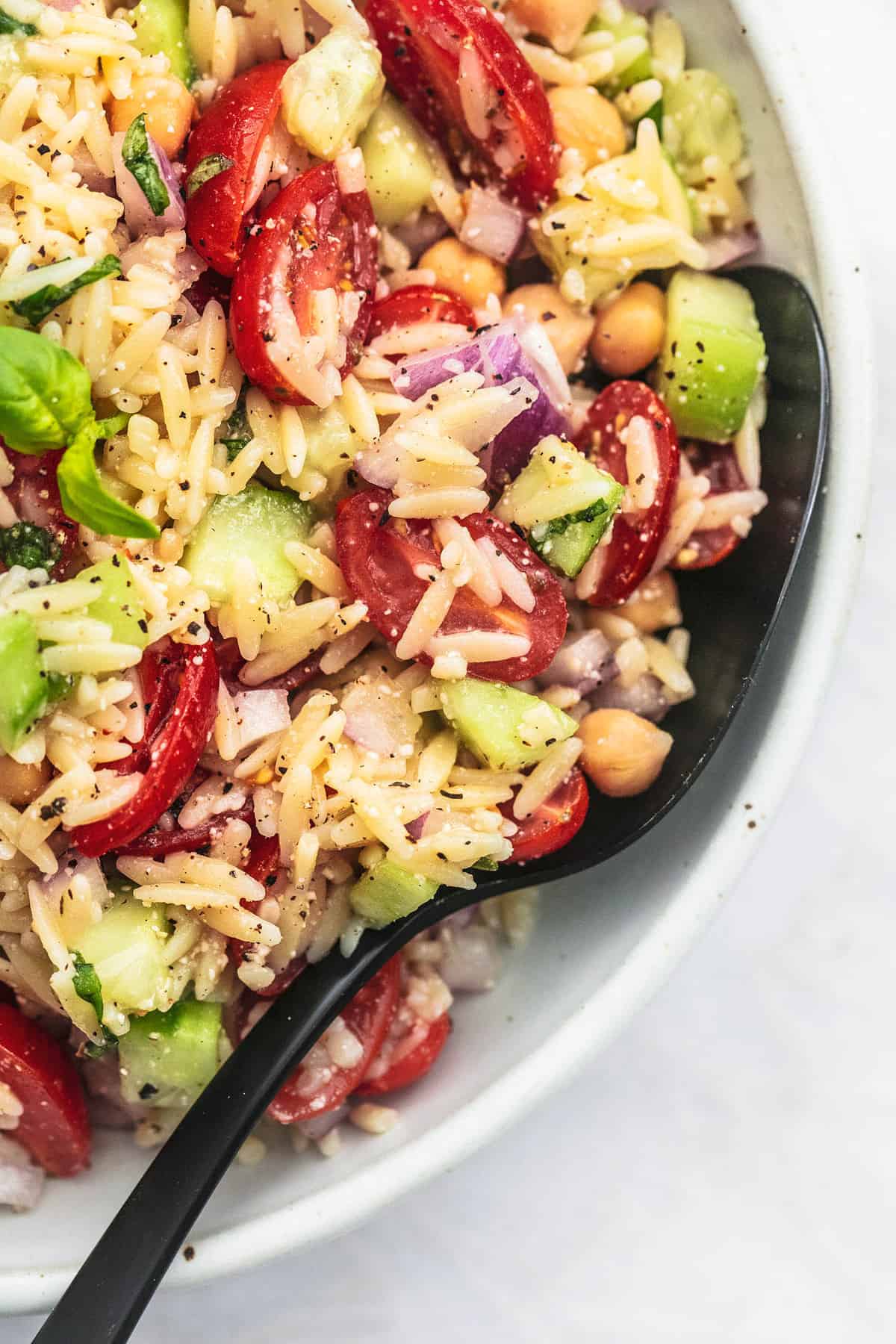 close up top view of Italian orzo salad with a serving spoon in a bowl.