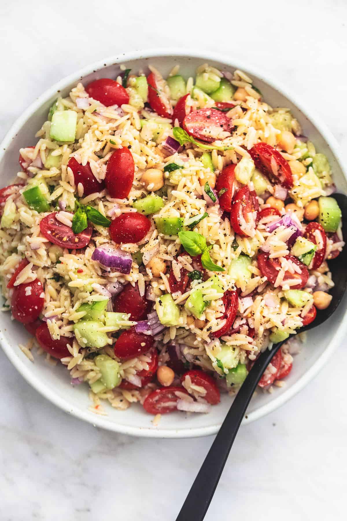 top view of Italian orzo salad with a serving spoon in a bowl.