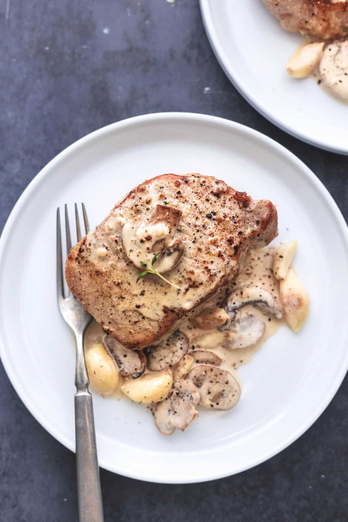 top view of a pork chop with creamy mushroom sauce and a fork on a plate.
