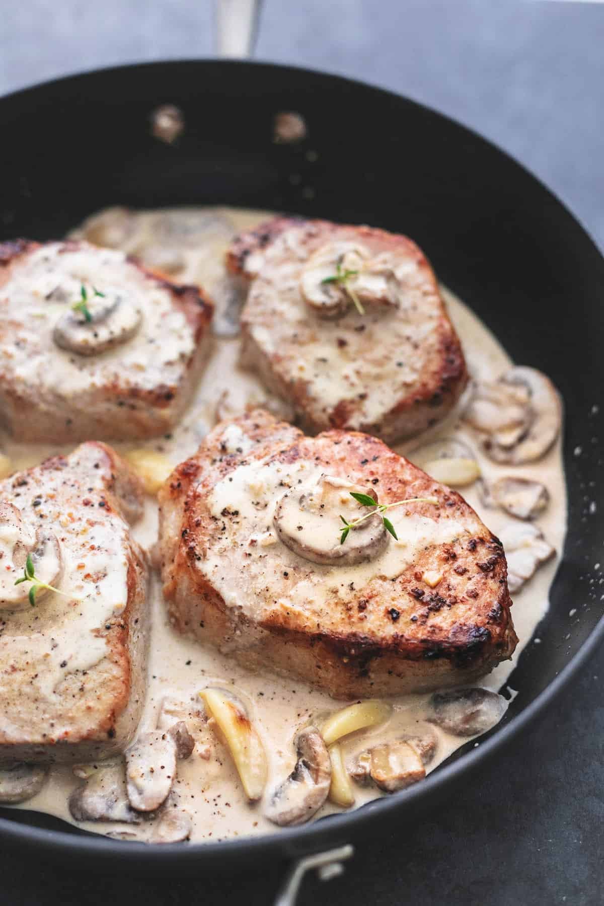 close up of baked pork chops with creamy mushroom sauce in a pan.