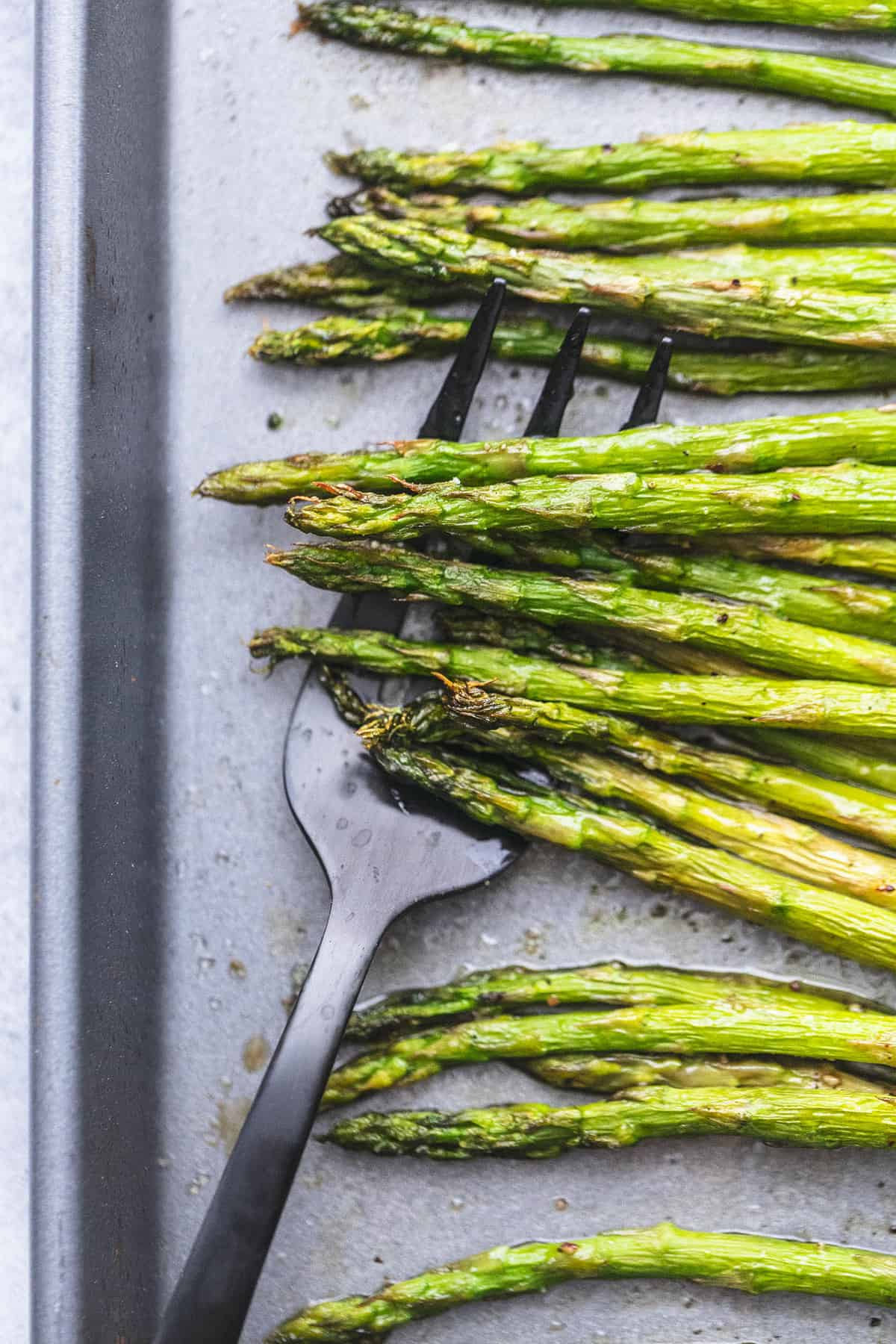 close up top view of roasted asparagus with a serving fork underneath on a baking sheet.