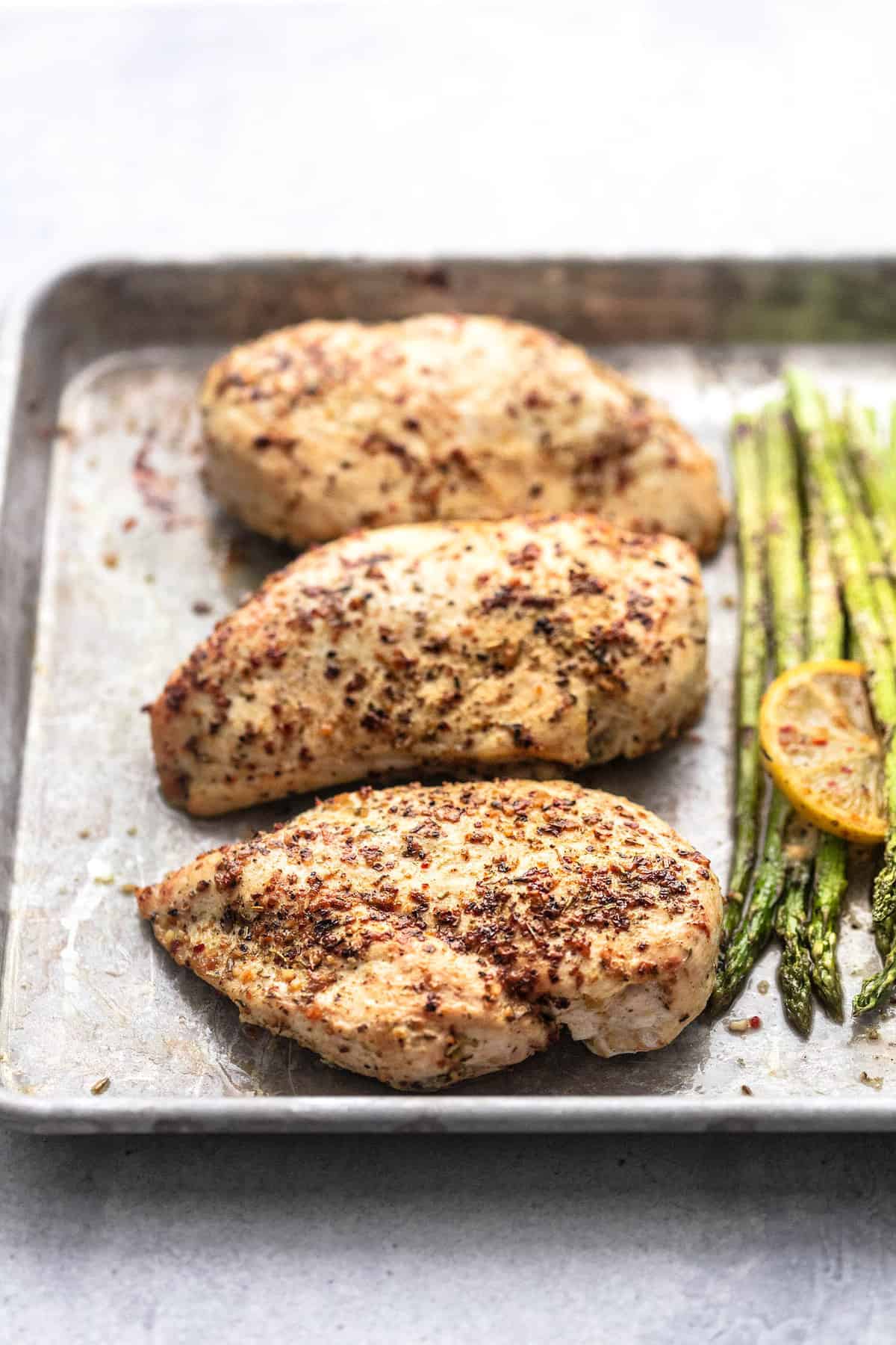 close up of chicken with asparagus barely visible on the side on a sheet pan.