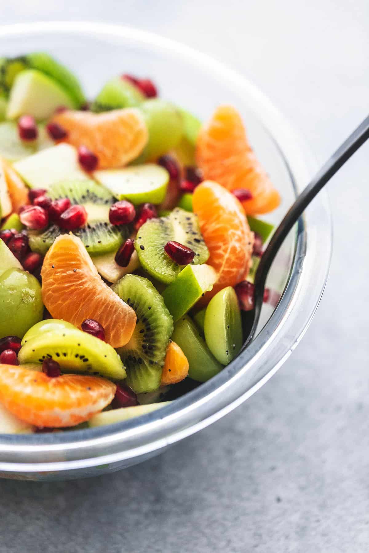close up of winter fruit salad with a serving spoon in a glass bowl.