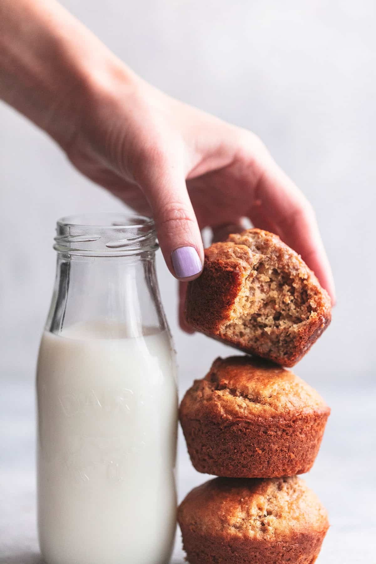 hand picking up a bran muffin with a bite out with a bottle of milk