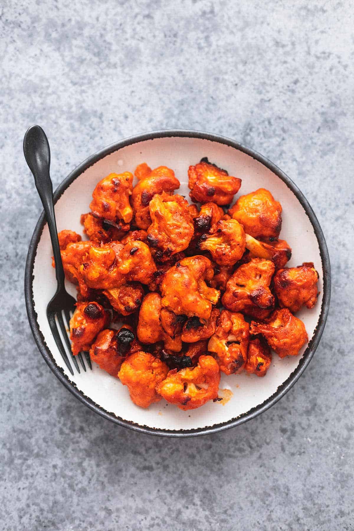 buffalo cauliflower on a white plate with a black fork on a gray table