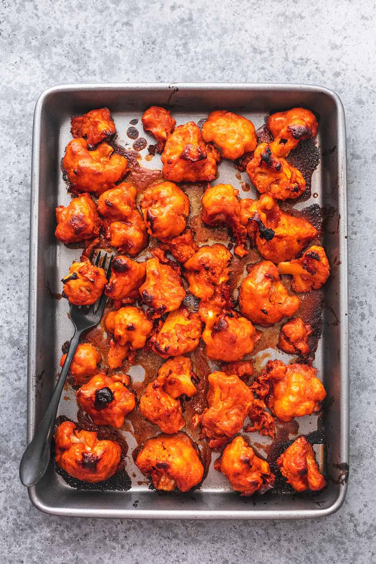 top view of buffalo cauliflower with a serving fork on a sheet pan.