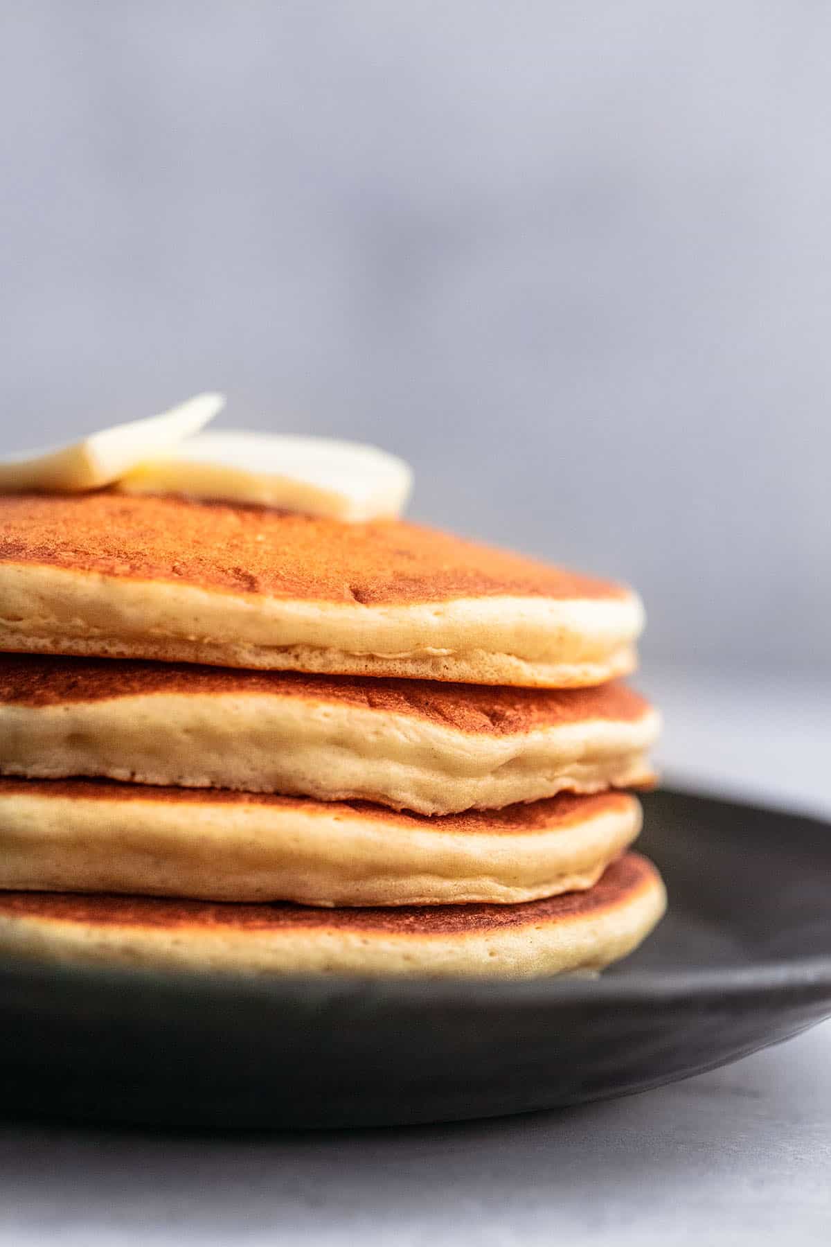 close up of butter on top of a stack of fluffy buttermilk pancakes on a plate.