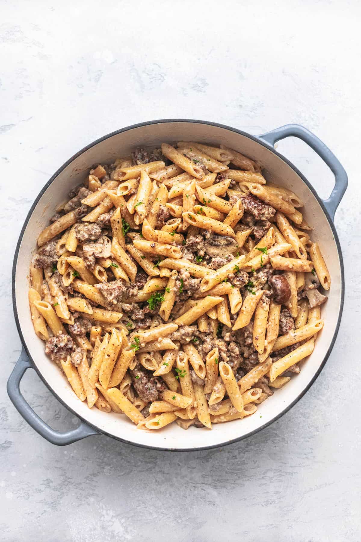 sausage and penne pasta noodles in a skillet on a gray background