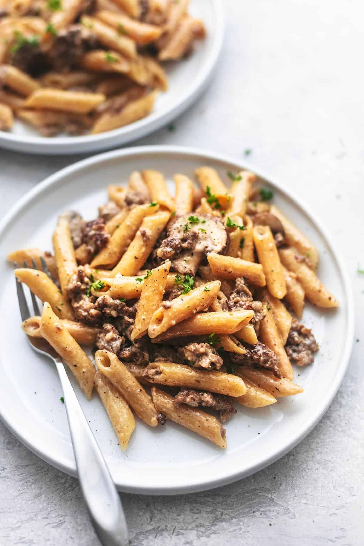 up close view of creamy sausage pasta with a fork on a plate with another plate in the background.