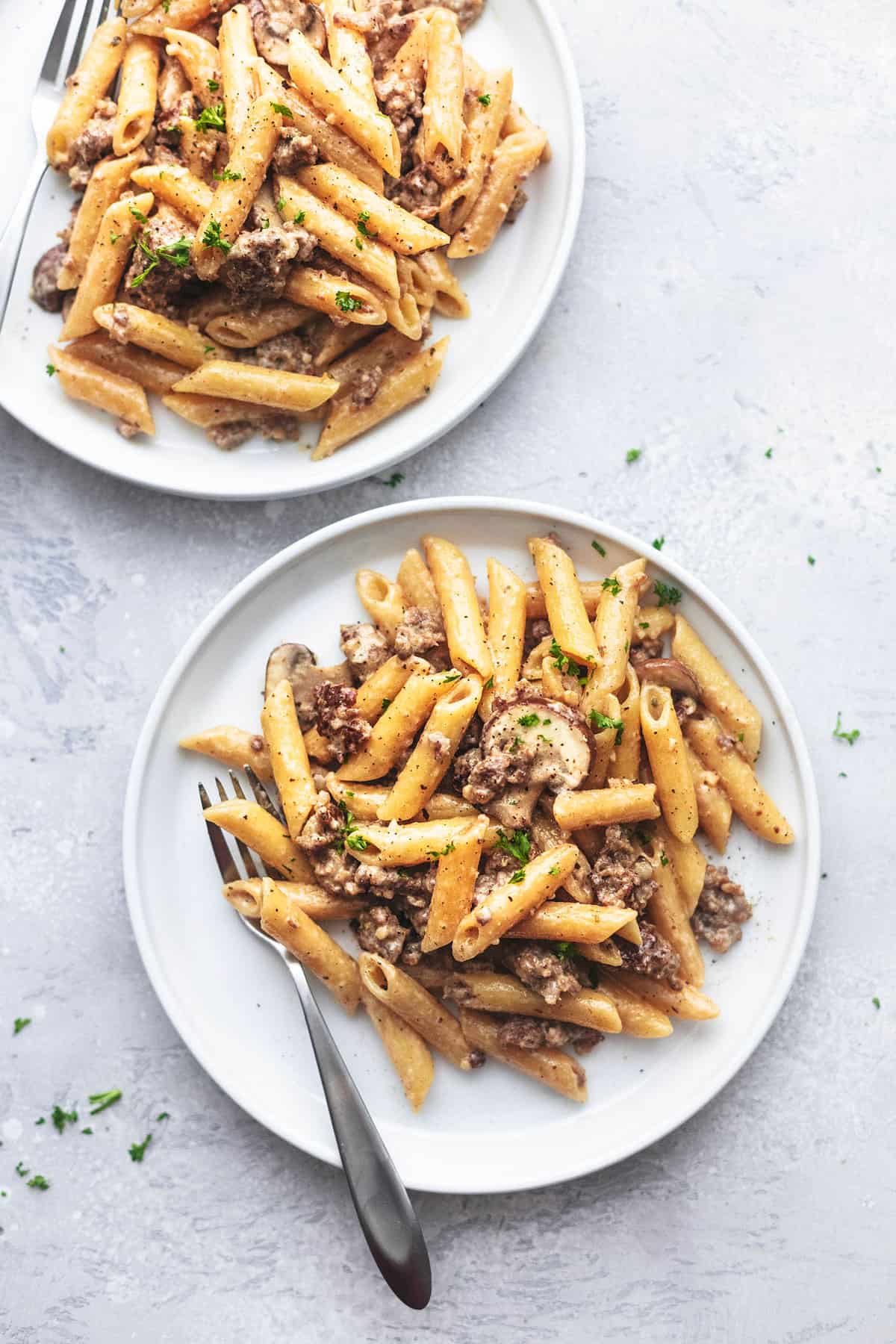 top view of creamy sausage pasta with forks on two plates on a gray background.