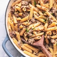 sausage and penne noodle pasta in a skillet with a wooden spoon