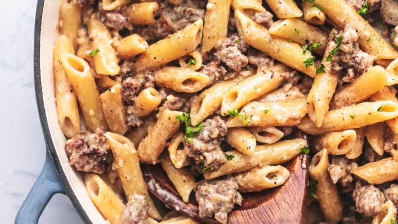 sausage and penne noodle pasta in a skillet with a wooden spoon