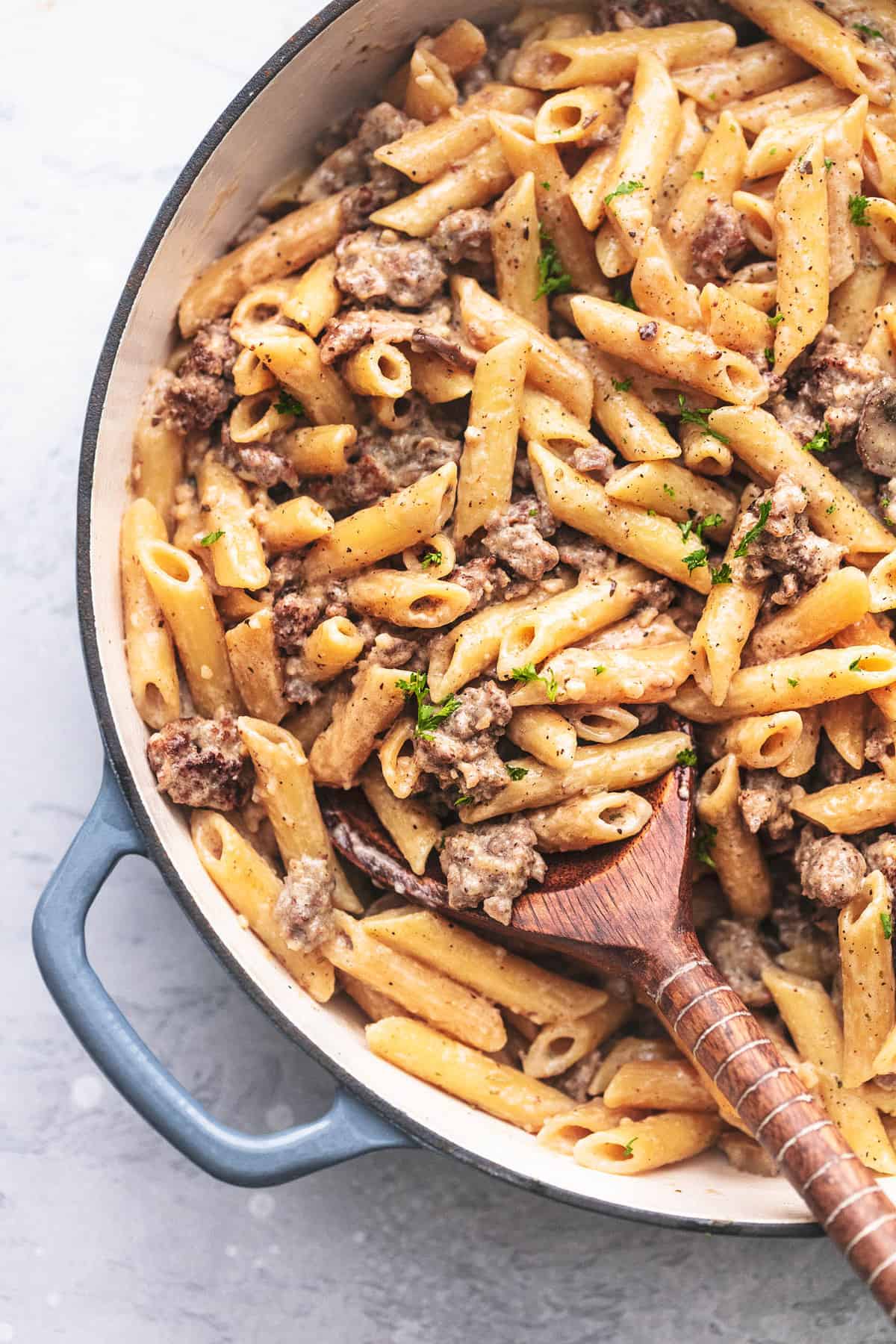 close up top view of creamy sausage and penne noodle pasta in a skillet with a wooden spoon.