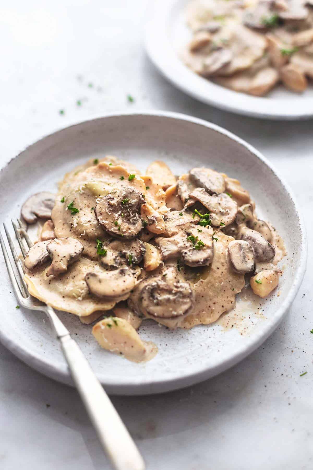 ravioli with mushroom cream sauce on a white plate with a fork.