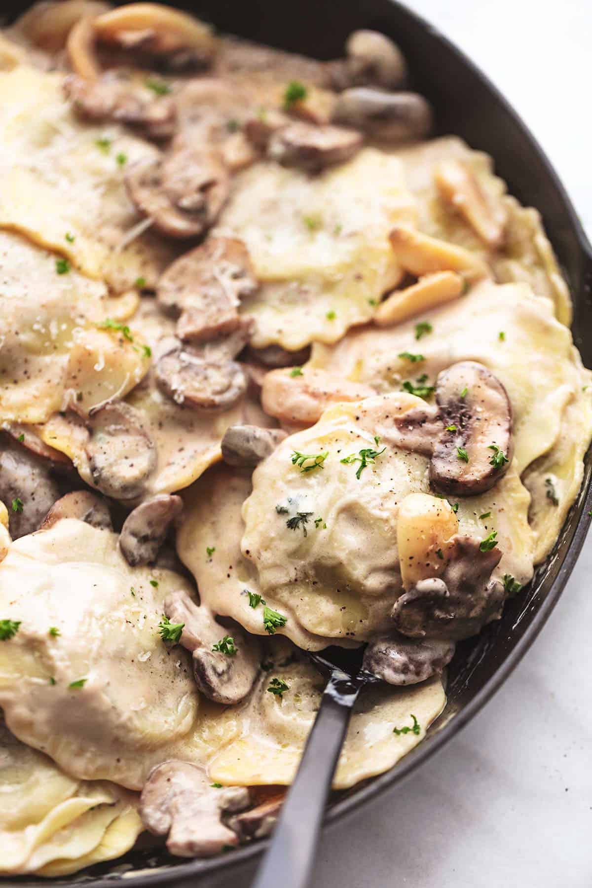 close up of ravioli with mushroom cream sauce with a spoon in a skillet.