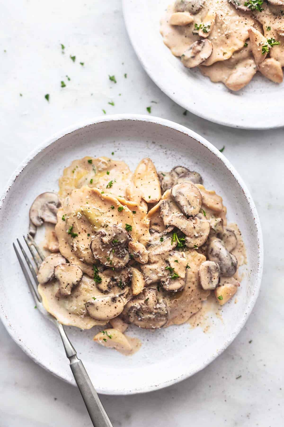 top view of ravioli with mushroom cream sauce on a white plate with a fork.