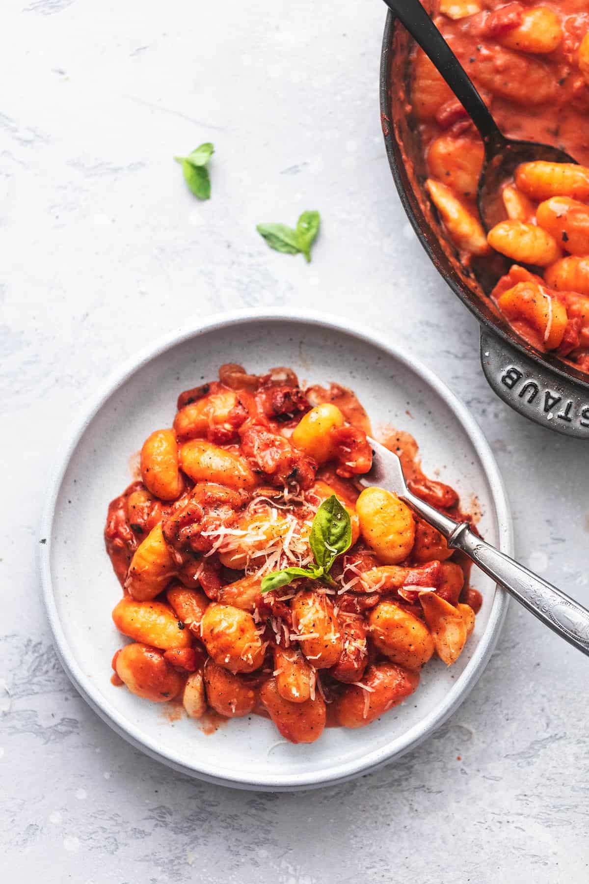 top view of gnocchi in tomato cream sauce with a fork on a plate with more in a skillet on the side.