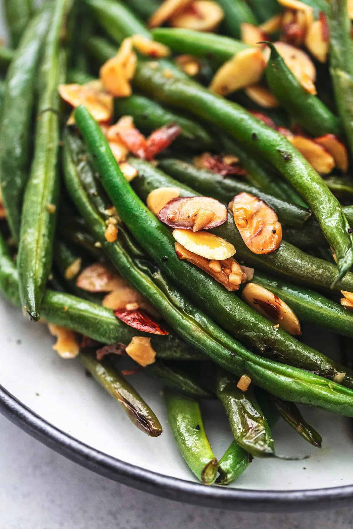 close up of sautéed green beans with garlic and almonds on a plate.