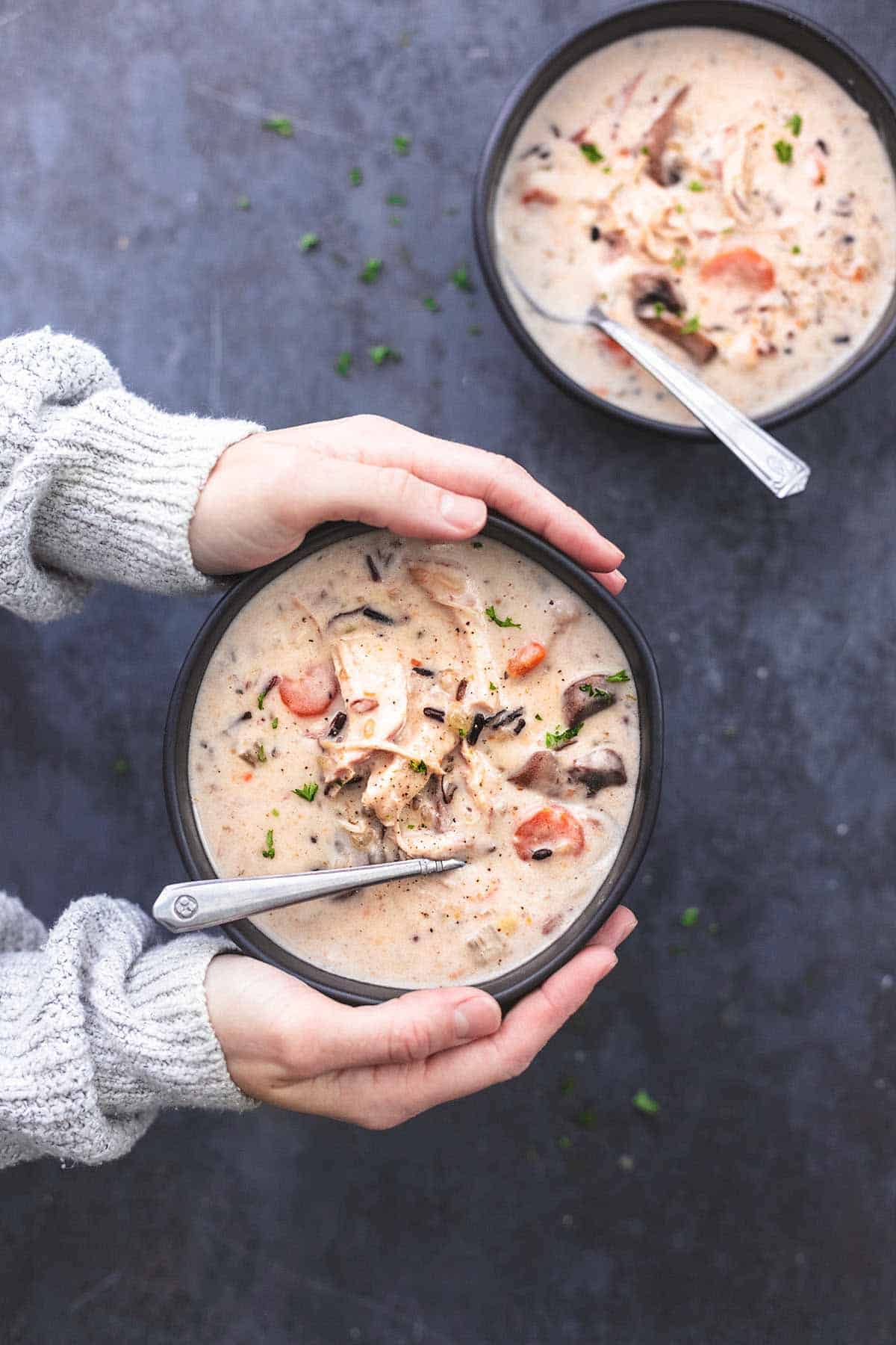 hands holding black soup bowl with chicken wild rice soup