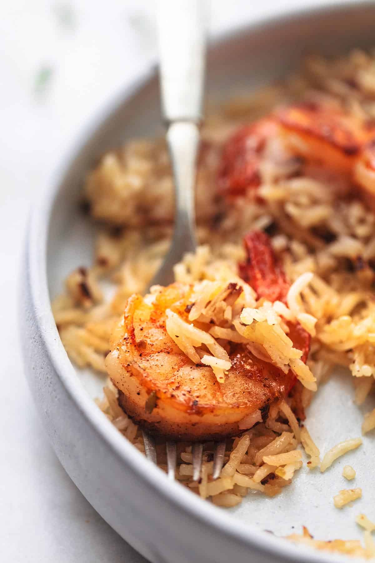 close up of a bite of lemon herb shrimp and rice skillet on a fork on a plate.