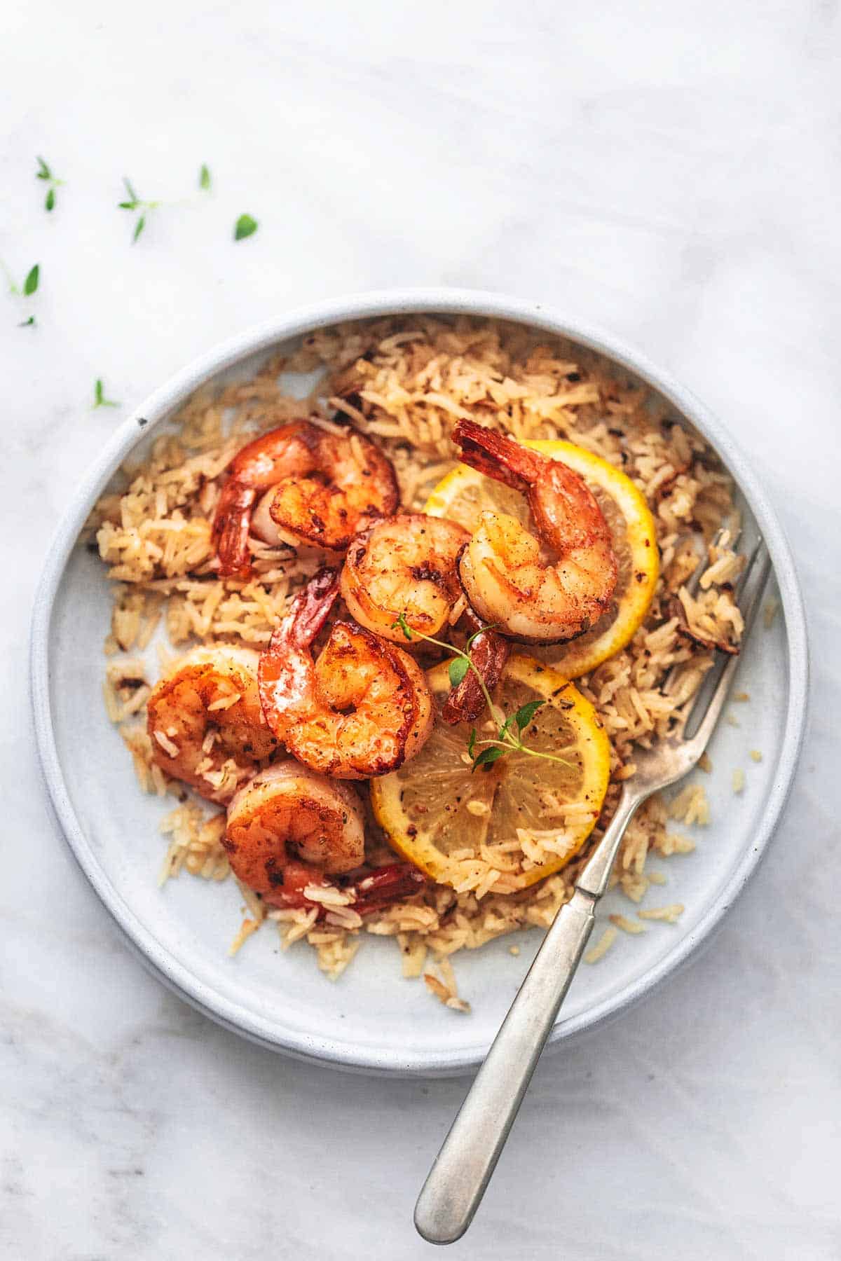 top view of lemon herb shrimp and rice skillet with lemon slices on a plate with a fork.