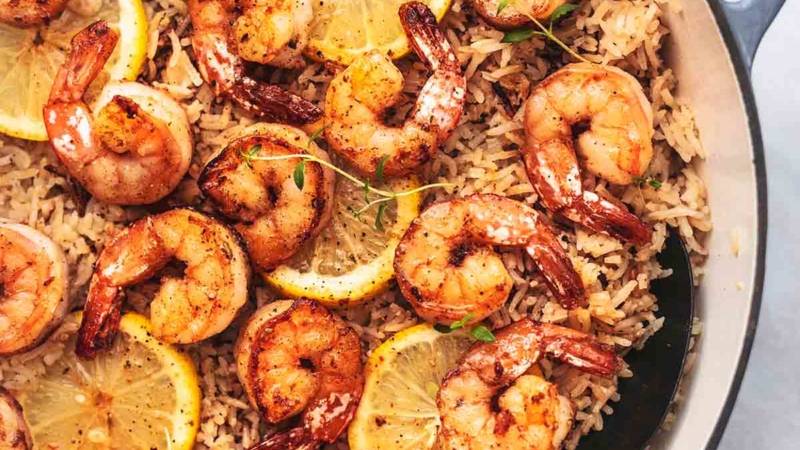 shrimp and rice with lemon slices in a skillet with a spoon