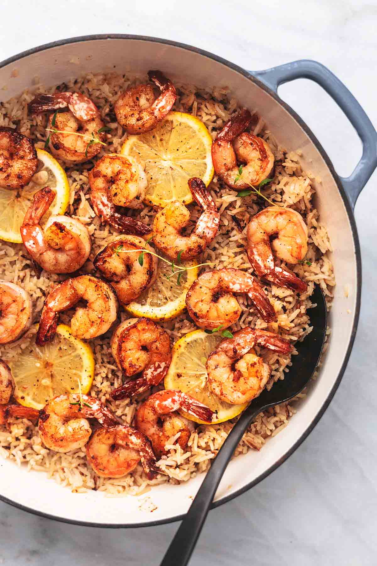 close up top view of lemon herb shrimp and rice skillet with lemon slices in a skillet with a serving spoon.