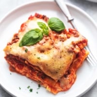 up close piece of lasagna topped with basil on a white plate with a fork