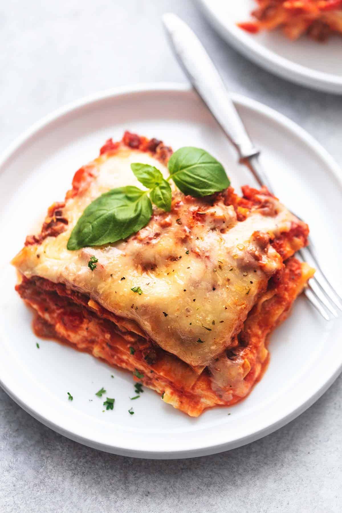 up close piece of lasagna topped with basil on a white plate with a fork