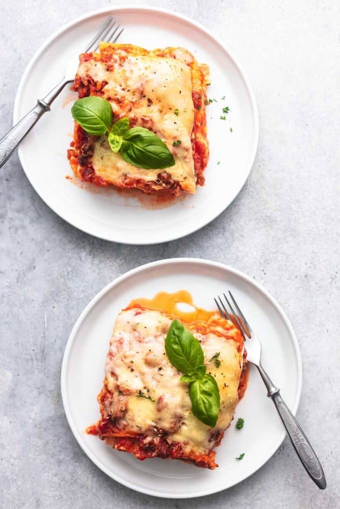 two plates of lasagna with forks on a gray background