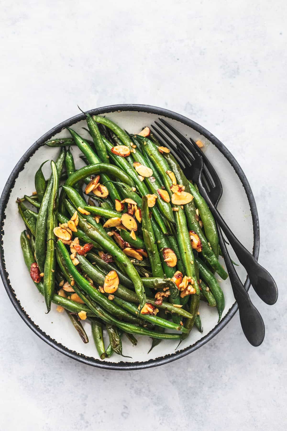 top view of sautéed green beans with garlic and almonds with two forks on a plate.