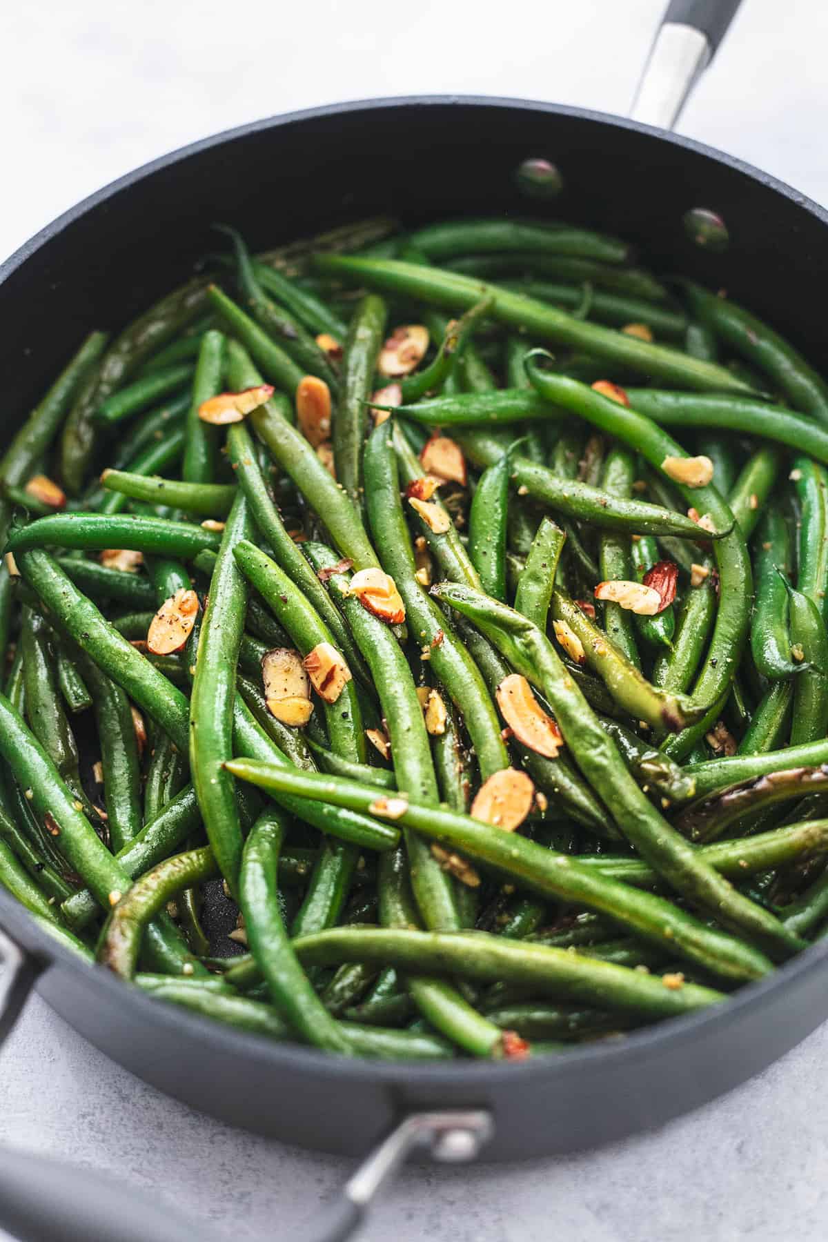 close up of sautéed green beans with garlic and almonds in a skillet.