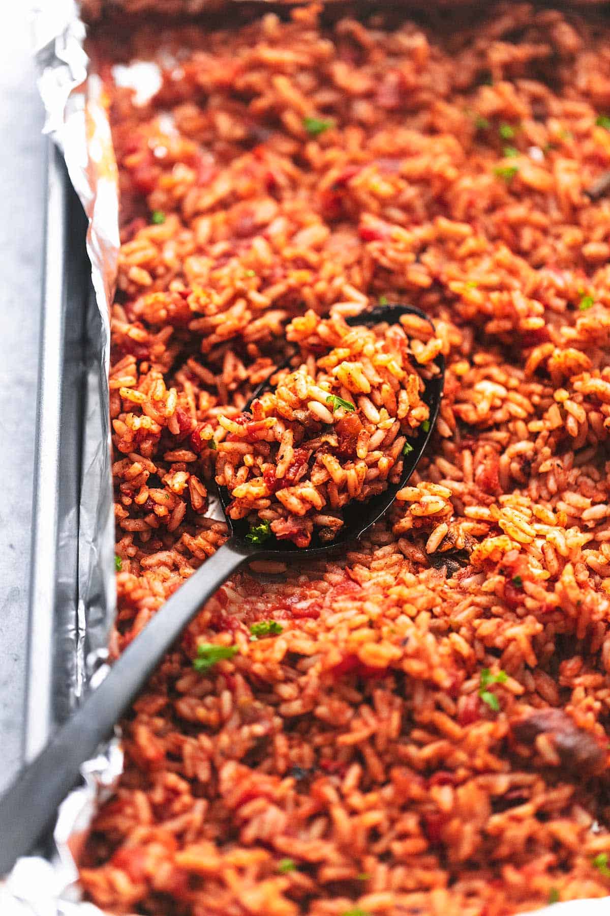 close up of Spanish rice with a serving spoon on a sheet pan.