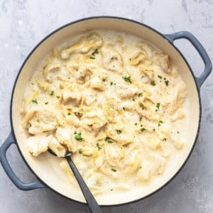 tortellini with alfredo sauce in a skillet with a serving spoon