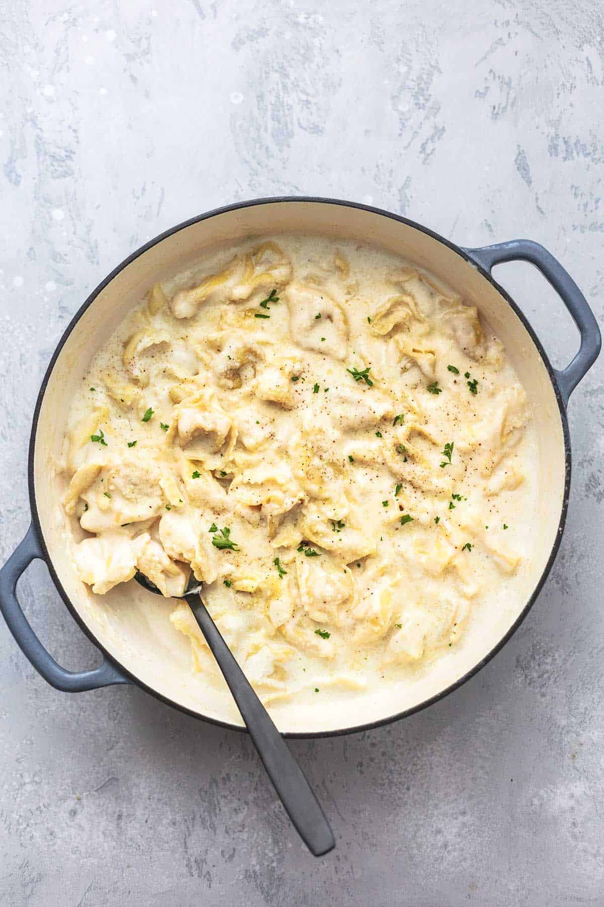 top view of tortellini alfredo in a skillet with a serving spoon.