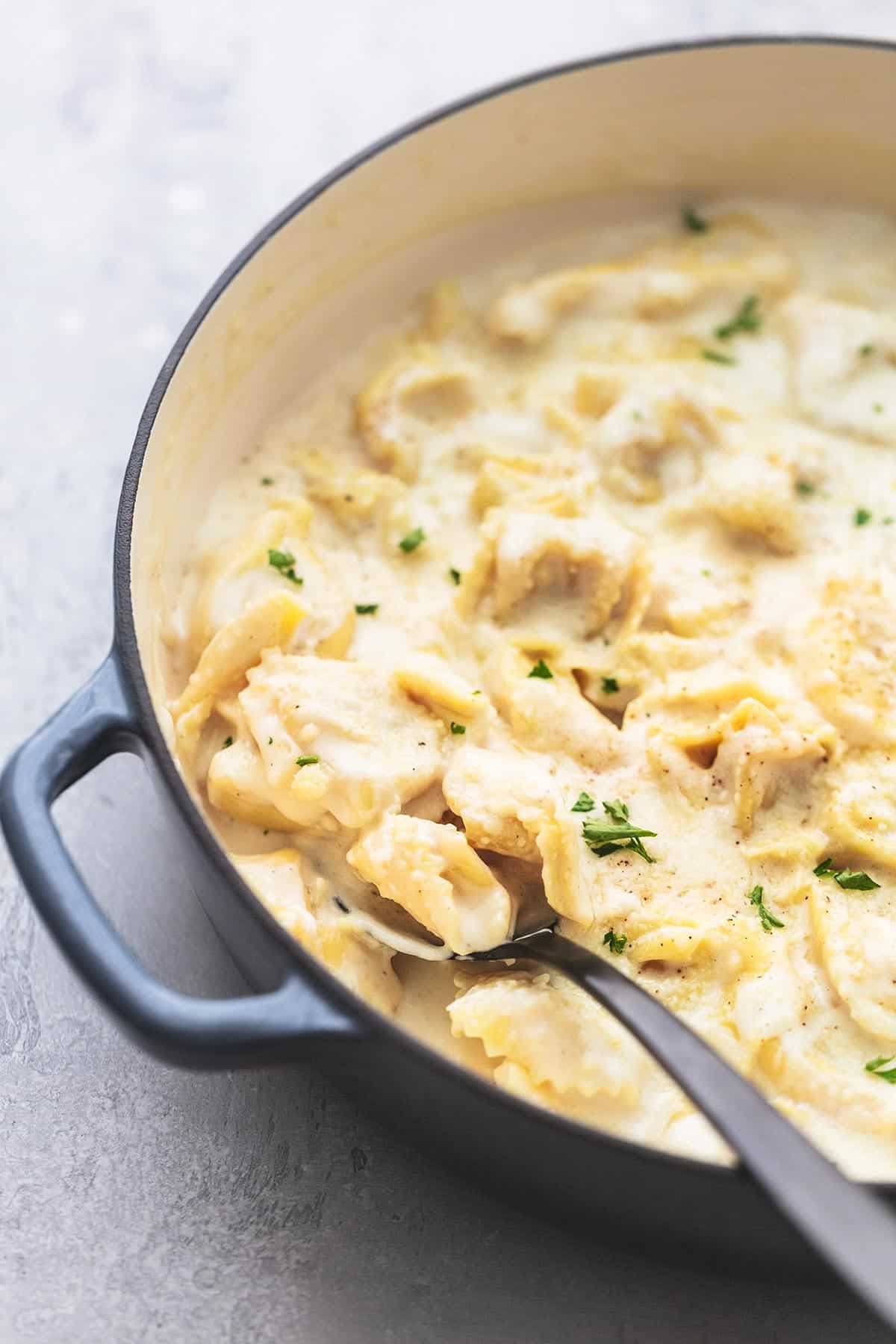 close up of tortellini alfredo with a serving spoon in a skillet.