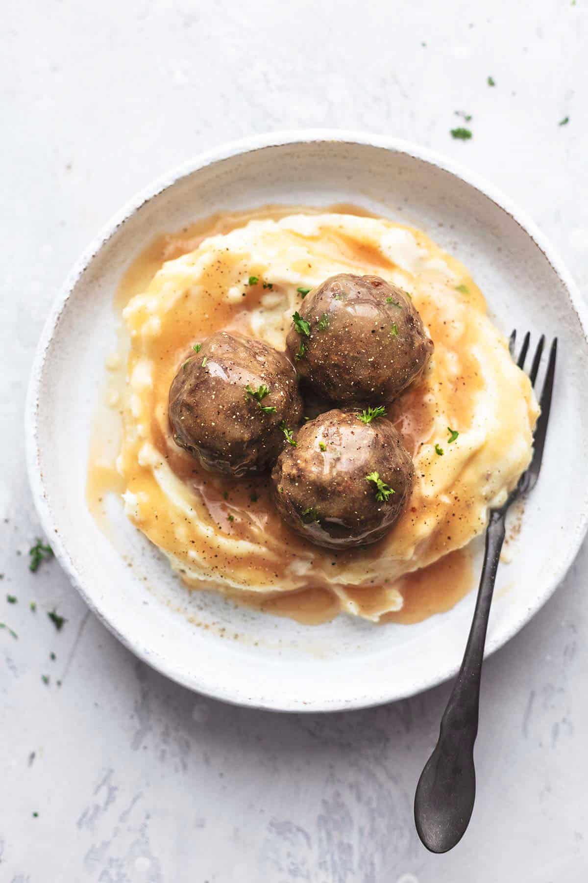 top view of meatballs on top of mashed potatoes and gravy with a fork on a plate.