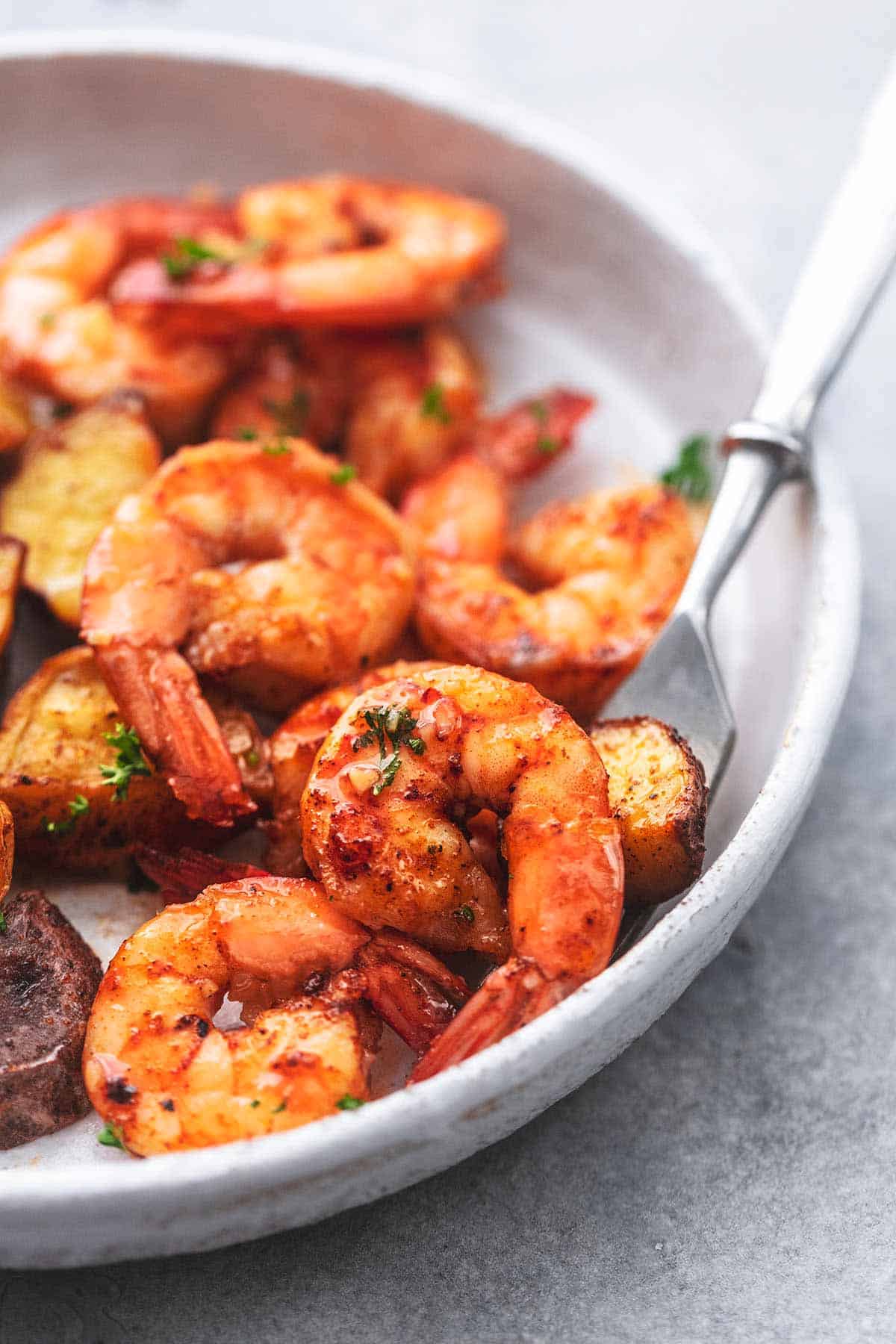 close up of shrimp with a fork underneath on a plate.