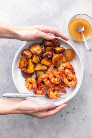 hands holding white plate with shrimp and potatoes