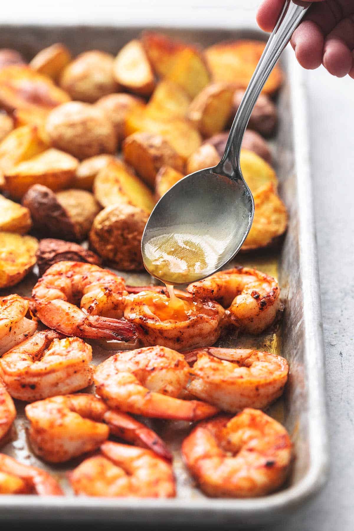 sheet pan cajun shrimp and potatoes on a sheet pan with a spoon drizzling butter over the shrimp.